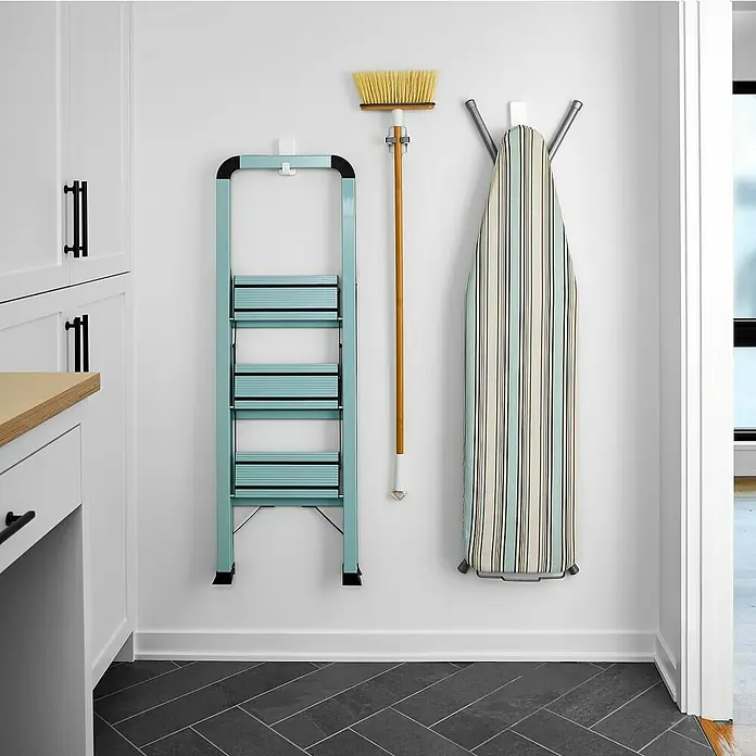 3M Command Gancho para colgar XL - Plástico, Blanco, 1 ud. - La imagen muestra una escalera de mano de color menta, una escoba y una tabla de planchar colgadas en una pared en un lavadero.