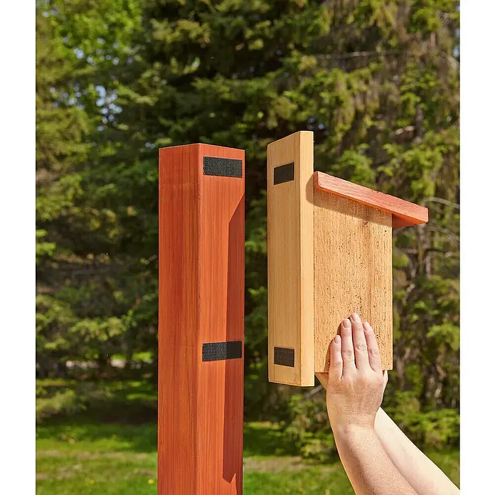 3M Scotch Cinta engomada Extreme - 25 mm x 1 m, Negro - Una casita para pájaros de madera con un techo rojo está unida a un poste de madera con velcro para colgarla y limpiarla fácilmente.