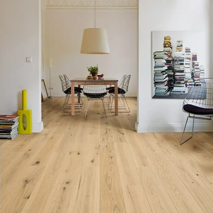 Living by Haro Parkett - Eiche Weiß strukturiert, Landhausdiele, 1.085 x 180 x 12 mm - Ein heller Holzboden erstreckt sich durch einen Raum, der mit einem Esstisch, Stühlen und Kunstwerken dekoriert ist.