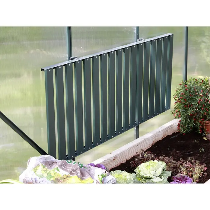 Vitavia Anzuchttisch - 56 x 120 x 81 cm, Smaragd - Das Bild zeigt ein grünes Lamellenfenster in einem Gewächshaus, das für Belüftung sorgt. Im Vordergrund sieht man Pflanzen und Blumenerde.