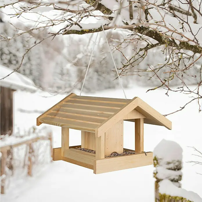 Windhager Vogelfutterhaus Rastkogel - 40 x 33 x 25 cm, Braun, Holz, Kiefer - Ein hölzernes Vogelhaus hängt an einem Ast im Schnee. Das Vogelhaus ist mit Vogelfutter gefüllt und bietet Vögeln einen Unterschlupf.