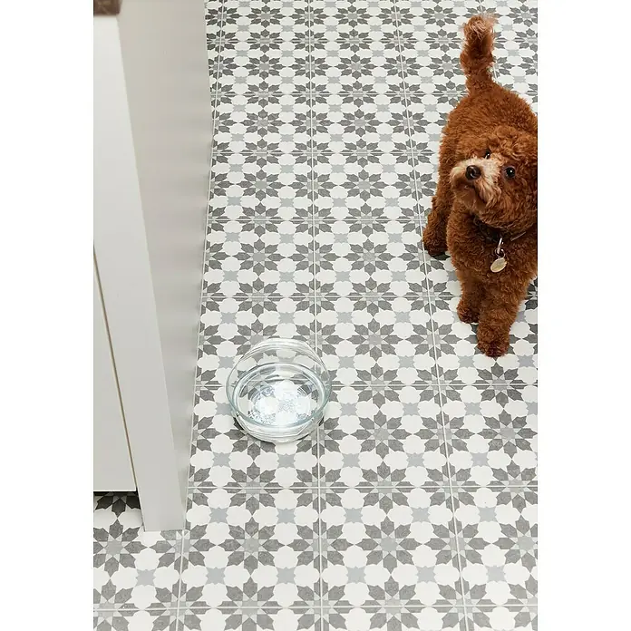 Beauflor PVC-Boden Meterware Artemis - 300 cm, Grau/Beige - Detailaufnahme des Musters einer Bodenfliese mit einem Hund und einer Wasserschüssel. Die Fliesen sind in Grau- und Weißtönen gehalten.