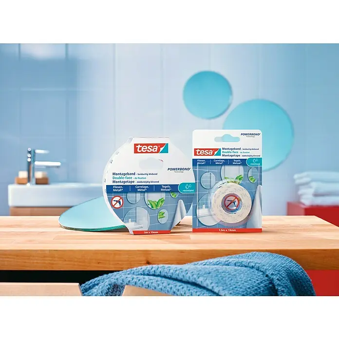 Tesa Powerbond Cinta de doble cara Resistente humedad - 1,9 cm x 5 m, Blanco - Cinta de montaje Tesa Powerbond para azulejos y metal, adhesiva de doble cara, expuesta sobre una mesa de madera con fondo de baño.