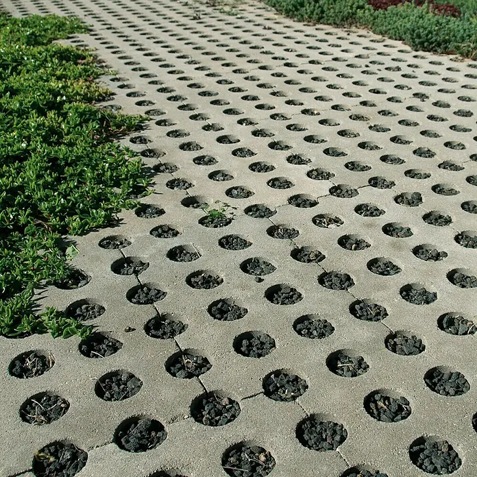 Adoquín para jardín - 60 x 36 x 8 cm, Gris, Hormigón - Adoquines ecológicos con aberturas circulares rellenas de grava oscura y exuberante vegetación verde que bordea la zona. Ideal para superficies permeables.