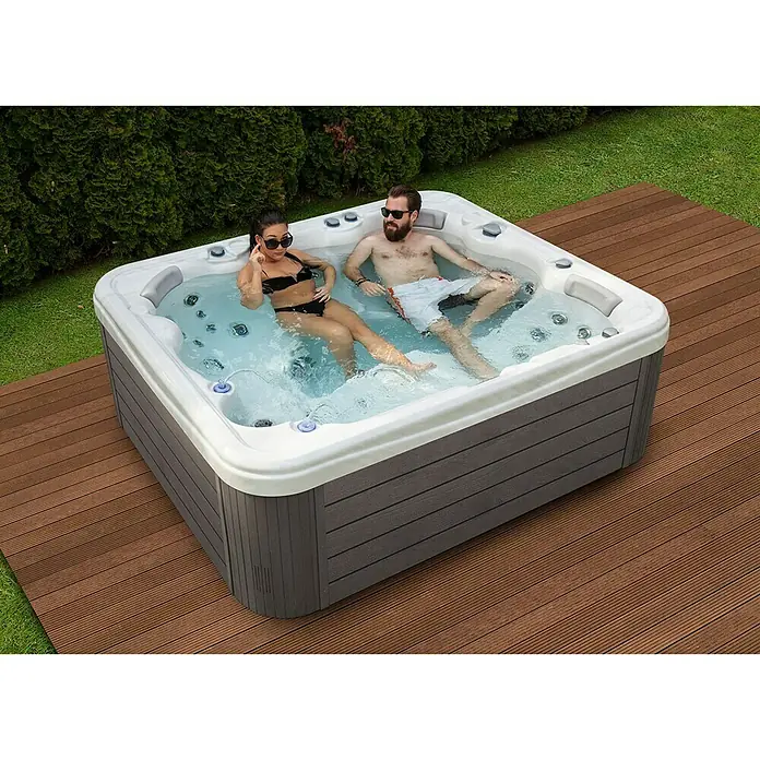 Camargue Außen-Whirlpool Serenity - 213 x 213 x 91 cm, Grau/Weiß, Max. Personenzahl: 6 - Ein luxuriöser Whirlpool im Garten, in dem ein Paar entspannt. Perfekt für die Entspannung im Freien mit stilvollem Design.