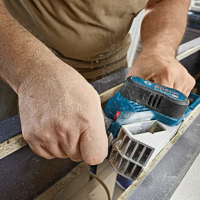 Bosch Professional Akku-Handhobel GHO 12V-20 - 12 V, Ohne Akku, 14.500 U/min - Nahaufnahme eines Bosch-Hobels in Aktion, der Holz bearbeitet und Späne erzeugt, ideal für Tischlerarbeiten.