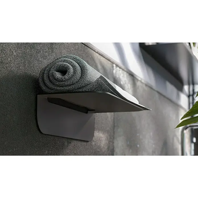 Camargue Antwerpen Ablage - Breite: 25 cm, Graphit, Matt - Eine zusammengerollte, graue Yogamatte liegt auf einem schwebenden Regal mit minimalistischem Design an einer strukturierten Wand.