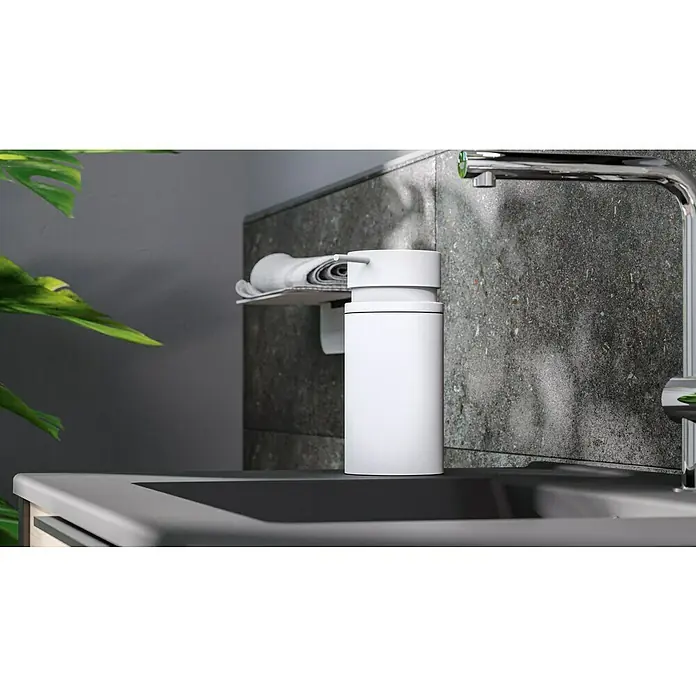 Camargue Antwerpen Seifenspender - Edelstahl, Weiß - Nahaufnahme eines weißen Seifenspenders auf einem Waschtisch, neben einem modernen Wasserhahn, mit grauem Hintergrund und einer grünen Pflanze im Vordergrund.