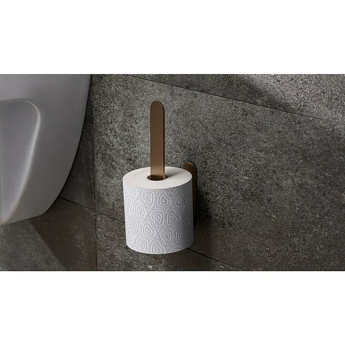 Camargue Antwerpen Ersatzpapierrollenhalter - Kupfer, Matt - Nahaufnahme eines stilvollen Toilettenpapierhalters mit einer Rolle weißen Papiers mit Herzmuster vor einer dunklen Steinwand.