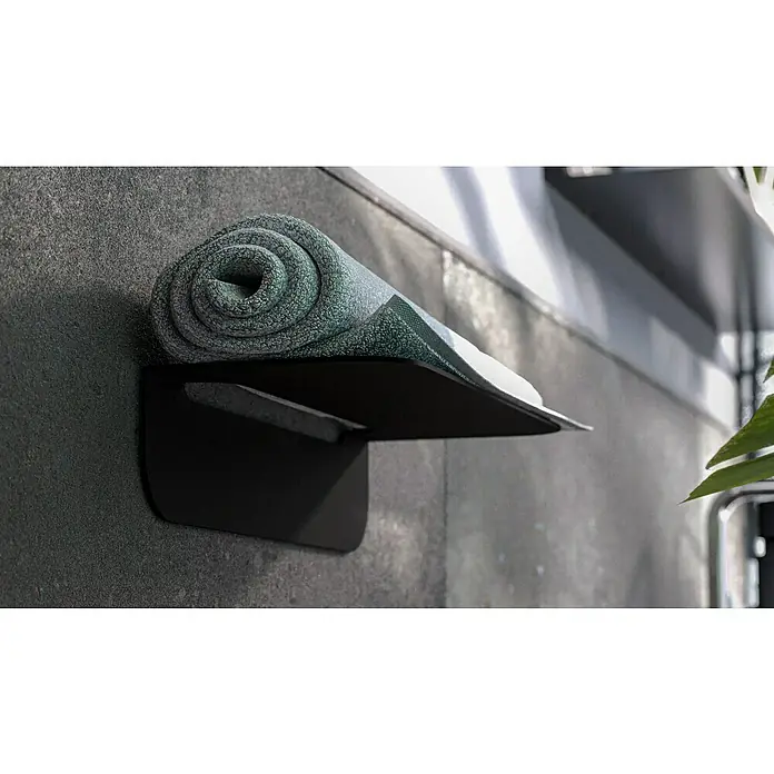 Camargue Antwerpen Ablage - Breite: 25 cm, Schwarz, Matt - Eine aufgerollte grüne Yogamatte liegt auf einem eleganten, mattschwarzen Wandregal vor einer grauen Wand, stilvoll und platzsparend.