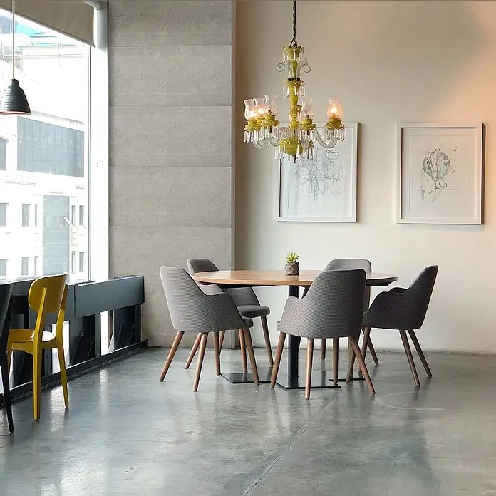 Nmc Decoflair Wandpaneel - Beton Light, 100 x 50 cm, Kunststoff - Ein heller Raum mit einem runden Holztisch und grauen Stühlen unter einem auffälligen grünen Kronleuchter, ergänzt durch Kunstwerke an der Wand.