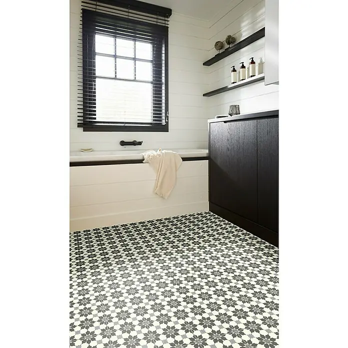 Beauflor PVC-Boden Meterware Artemis - 300 cm, Grau/Beige - Badezimmeransicht mit gemusterten Bodenfliesen, weißer Wannenverkleidung, dunklen Akzenten und Fenster mit Jalousien für ein modernes Design.