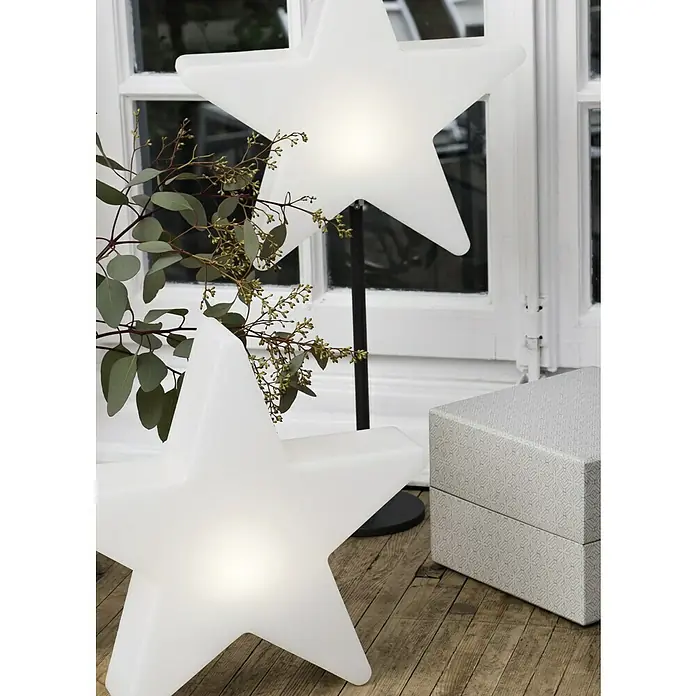 8 Seasons Design Shining LED-Stern Star - Außen, 10 cm, Neutralweiß - Dekorative LED-Sternleuchten auf einem Holzboden, die eine warme Atmosphäre schaffen. Eine Geschenkbox und ein Fenster im Hintergrund ergänzen das Ambiente.