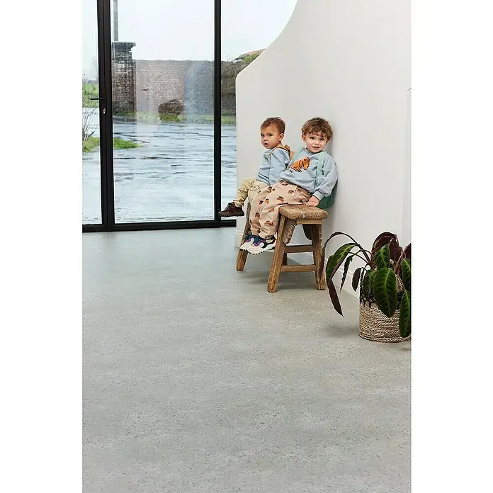 Beauflor PVC-Boden Meterware Themis - Steinoptik, Breite: 400 cm, Anthrazit/Schwarz - Zwei Kinder sitzen auf einem Hocker. Beide tragen Pullover mit Tiermotiven und gemusterte Hosen.