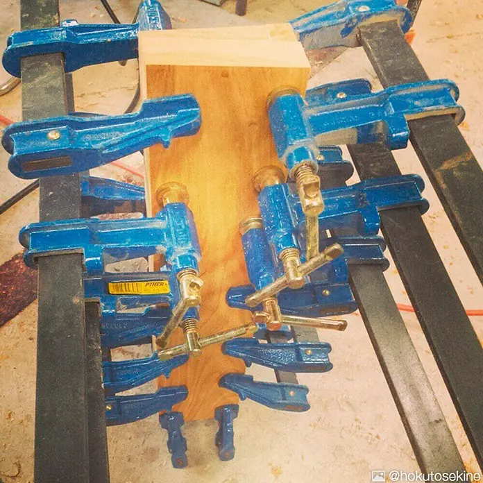 Piher Sargento E-30 - Anchura de sujeción: 300 mm, Fuerza de tensión: 9.000 N, Apertura máxima: 85 mm - Detalle de varias abrazaderas azules presionando madera, posiblemente para encolar o asegurar. Las abrazaderas son robustas y fáciles de usar.