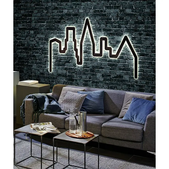 Paulmann LED-Band FlexLED 3D Basisset - Länge: 1,5 m, Lichtfarbe: Warmweiß, 6,5 W, 480 lm - Ein modernes Wohnzimmer mit einem grauen Sofa und einer beleuchteten Skyline-Wanddekoration, die eine gemütliche Atmosphäre schafft.