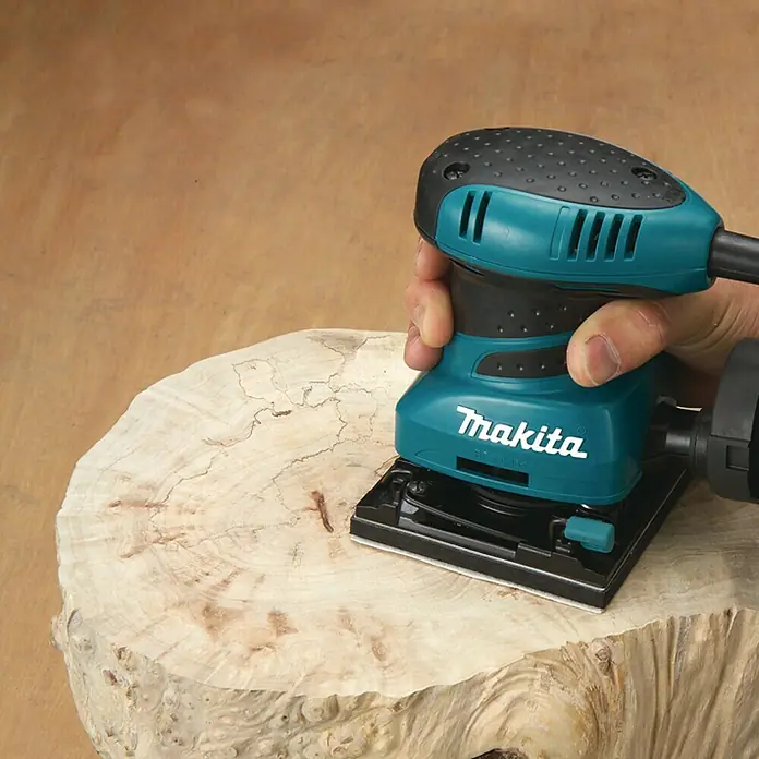 Makita Elektro-Schwingschleifer BO4555J - 200 W - Nahaufnahme eines Makita-Schleifgeräts beim Bearbeiten eines Holzstücks.