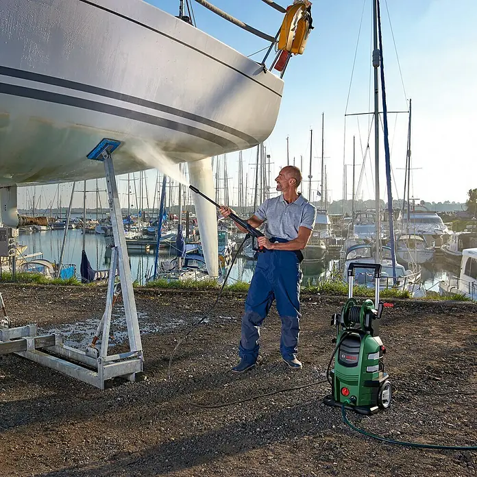 Bosch Hochdruckreiniger AdvancedAquatak 160 - 2.600 W, Max. Druck: 160 bar, Fördermenge: 570 l/h - Ein Mann benutzt einen Bosch Hochdruckreiniger, um ein Boot zu reinigen. Der Hochdruckreiniger ist grün und schwarz und steht auf einem Kiesweg.