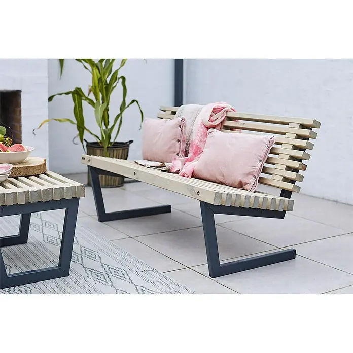 Plus Gartenbank Siesta - B x T x H: 140 x 49 x 43 cm, Nadelholz, Schiefergrau, Natur - Eine stilvolle Gartenbank aus Holz und Metall mit rosa Kissen und einer Decke auf einer Terrasse.