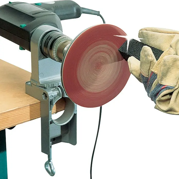 Wolfcraft Soporte de taladro - Apertura máxima: 60 mm - Primer plano de una esmeriladora de banco con un disco de lijado rojo, y una mano enguantada está lijando.