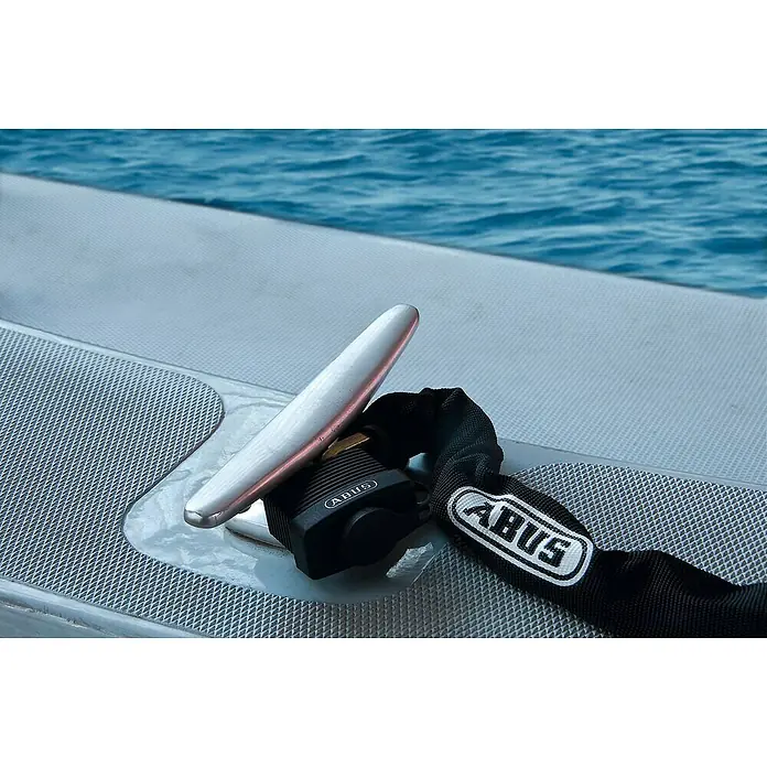 Abus Candado 70AL - An x Al: 49 x 68 mm, 1 ud., Aluminio - Cadena ABUS con un candado asegura un objeto en un barco, con el océano al fondo.
