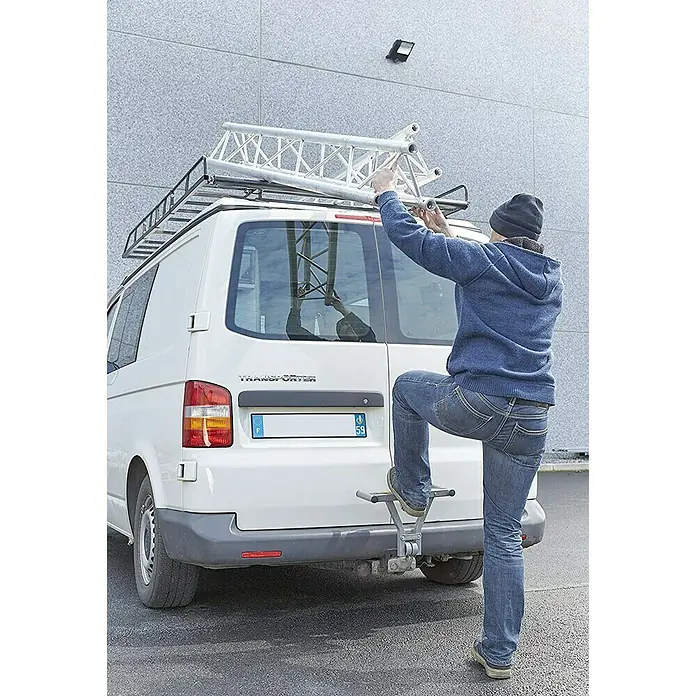 Mottez Dispositivo antirrobo A084C - L x An x Al: 40 x 27 x 16 cm - Una persona sube a un escalón de enganche para trabajar en una VW Transporter blanca con baca y escalera. Práctico acceso.