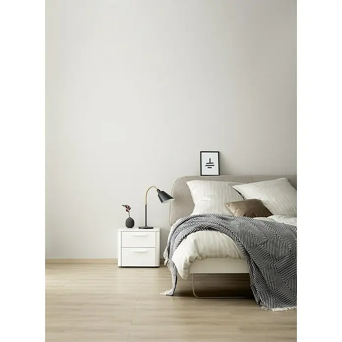 SCHÖNER WOHNEN-Farbe Wandfarbe DesignfarbeSanftes Seidengrau, Matt, 100 ml, Konservierungsmittelfrei - Schlafzimmer-Interieur mit Bett, Nachttischlampe und dekorativem Schwarz-Weiß-Überwurf für eine gemütliche Atmosphäre.