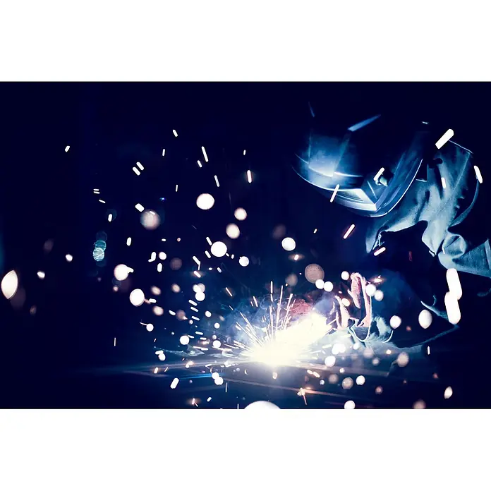 Gys Soldador combinado GYSMI E163 - Corriente de soldadura: 10 A - 160 A - Un soldador con equipo de protección trabajando, chispas volando y luz iluminando la escena. Soldadura profesional en el trabajo.