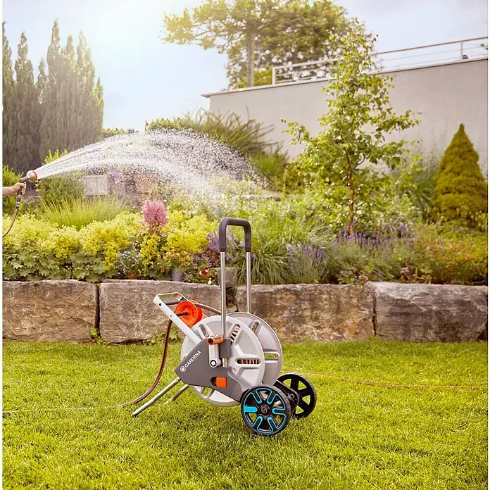 Gardena Schlauchwagen CleverRoll L Easy - Metall, Schlauchkapazität: 100 m, 13 mm (½″) - Gardena Schlauchwagen im Einsatz, umgeben von einem üppigen Garten, der bewässert wird. Praktische Gartenbewässerung mit diesem robusten Helfer.