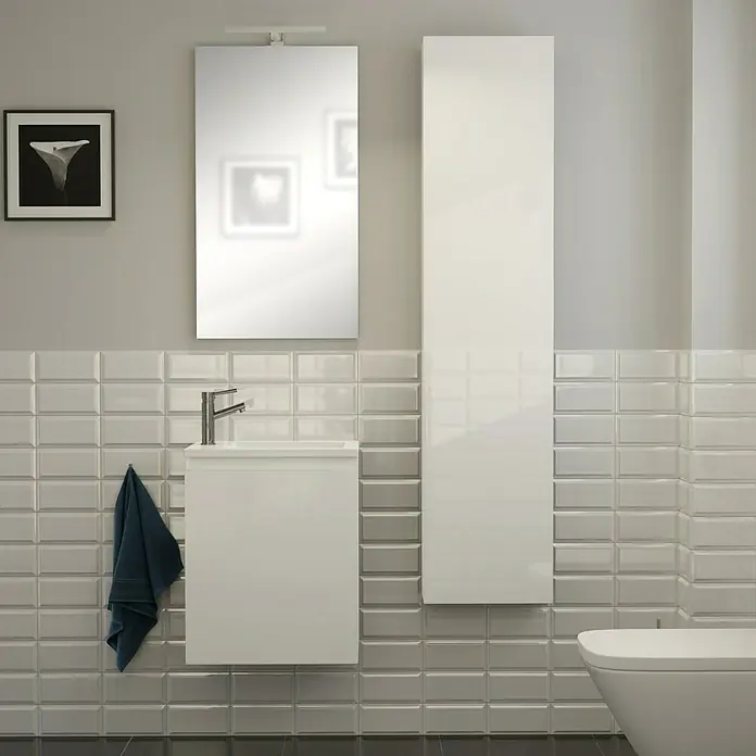 Camargue Espacio Badmöbel-Set H43 - 90 cm, Gama weiß glänzend - Badezimmer-Interieur mit einem modernen weißen Waschtischunterschrank, einem hochglänzenden Spiegelschrank und einer Toilette vor grauem Fliesenspiegel.