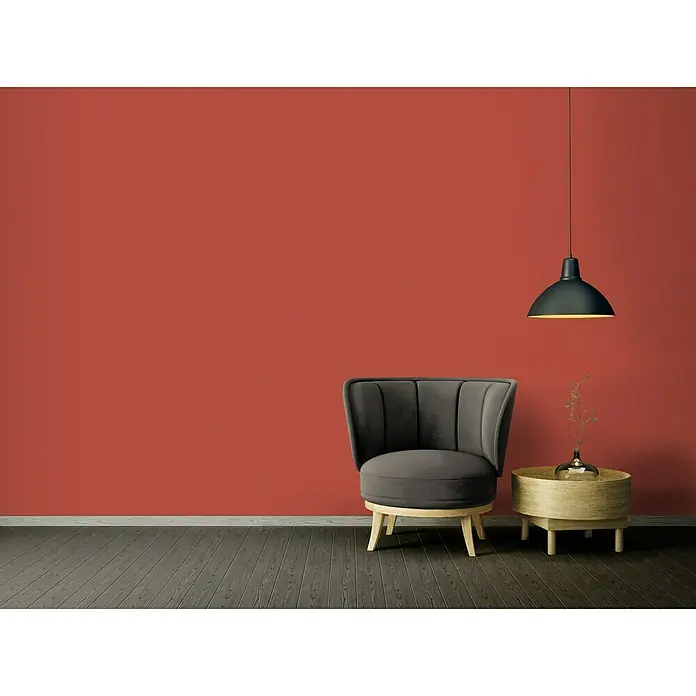 A.S. Création Ethnic Origin Vliestapete - Rot, Uni, 10,05 x 0,53 m - Stilvoller, grauer Sessel mit passendem Beistelltisch und Hängelampe vor einer roten Wand. Elegantes Möbelstück für modernes Wohnambiente.