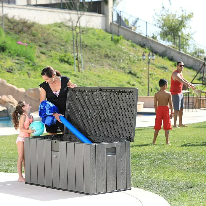 Lifetime Gartenbox - L x B x H: 151 x 72 x 69 cm, Kunststoff, 570 l, Dunkelgrau - Eine Familie beim Verstauen von Poolzubehör in einer grauen Aufbewahrungsbox im Freien. Praktisch und stilvoll!