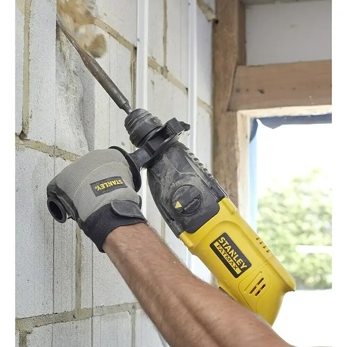 Stanley FatMax Martillo combinado SFMEH200K-QS - 750 W, 2,2 J, Alojamiento SDS-Plus - Primer plano de un martillo rotativo Stanley Fatmax amarillo perforando una pared, también muestra guantes y brazo de trabajo.