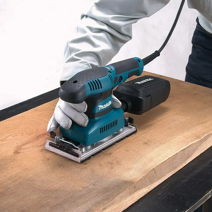 Makita Lijadora orbital eléctrica BO3711 - 190 W - Primer plano de una lijadora orbital Makita en acción, utilizada sobre una pieza de madera. Perfecto para proyectos de bricolaje y profesionales.