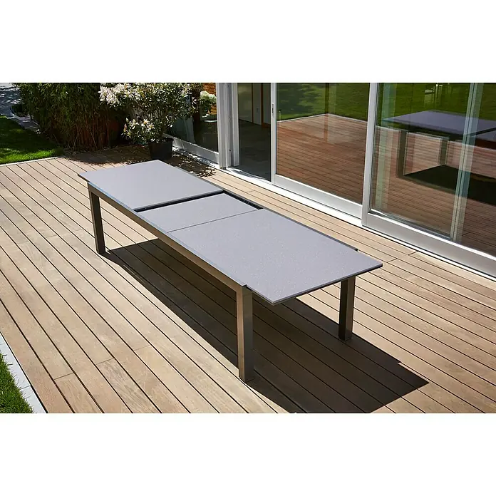 Sunfun Maja Mesa de jardín XL - L x An x Al: 280 x 100 x 75 cm, Aluminio, vidrio, Rectangular, Antracita, Extensible - Una mesa extensible de metal gris con una superficie lisa se encuentra en una terraza de madera al aire libre.
