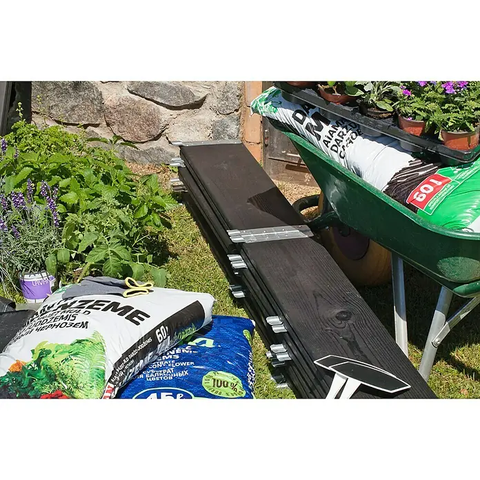 Gardol Hochbeetumrandung Palettenrahmen - L x B x H: 120 x 80 x 20 cm, Holz, Schwarz - Eine Nahaufnahme von Gartenutensilien, darunter Pflanzenerde, Blumen und Holzbretter, die für Gartenprojekte bereitliegen.