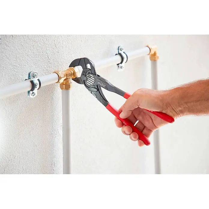Wiha Wasserpumpenzange - Länge: 25 cm - Hand benutzt schwarze Wiha Zange mit roten Griffen, um ein Messingfitting an weißen Rohren zu verstellen.