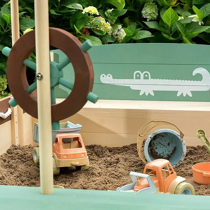 Muddy Buddy Sandkasten Jungle King - L x B x H: 195 x 110 x 120 cm, Holz - Eine Nahaufnahme einer hölzernen Sandkiste mit Spielzeugautos und einem Eimer, mit einem dekorativen Krokodil an der Seite.