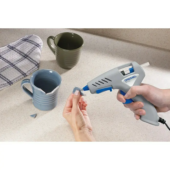 Dremel Heißklebepistole 910-3 - Aufheizzeit: 5 min, Durchmesser Klebepatrone: 7 mm - Nahaufnahme einer Person, die ein Stück eines zerbrochenen Keramikbechers mit einer Dremel 910 Heißklebepistole anklebt.