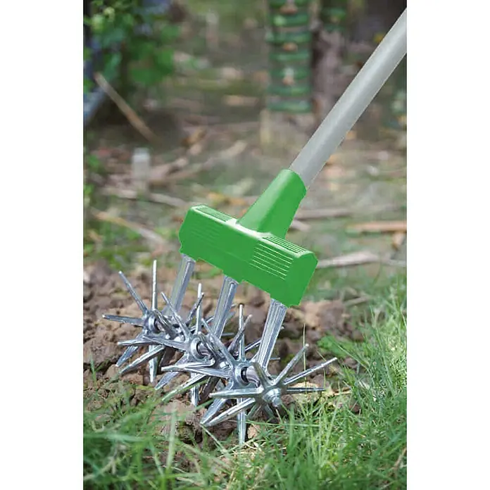 Freund Victoria Rollkultivator - Arbeitsbreite: 15 cm, Länge Stiel: 100 mm - 158 mm, Teleskopstiel, Stahl - Das Bild zeigt einen manuellen Vertikutierer mit einem grünen Griff und silbernen Metallrädern, der in einem Garten verwendet wird.