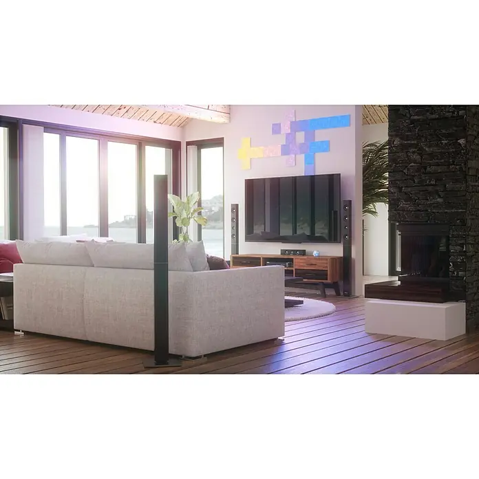 Nanoleaf Erweiterungskit Canvas 4 Panels - 4 Stk., 4 W, Weiß, RGBW, Canvas, Smart Home-fähig: Ja - Das Bild zeigt ein modernes Wohnzimmer mit einem grossen Sofa, einem Fernseher und farbigen Lichtpaneelen an der Wand, die für eine angenehme Atmosphäre sorgen.