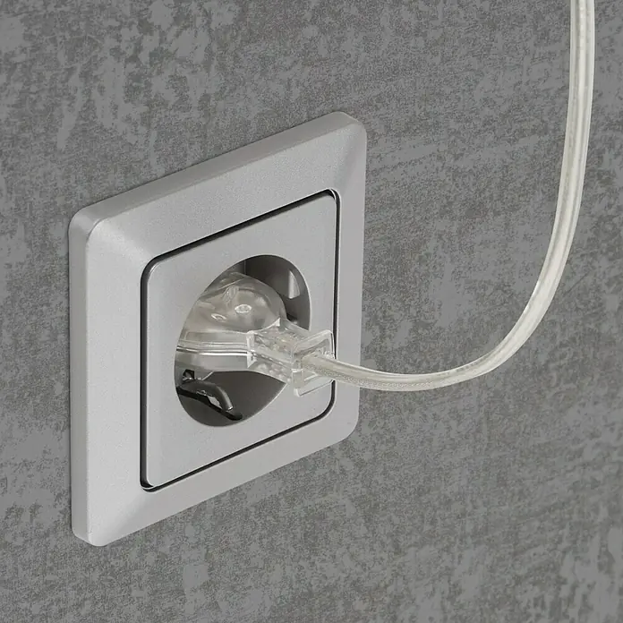 Briloner LED-Wandstrahler Tuso - 4 W, L x B x H: 5,8 x 21,7 x 40,3 cm, Warmweiß - Nahaufnahme einer Steckdose mit eingestecktem transparentem Stecker an einer grauen Wand.
