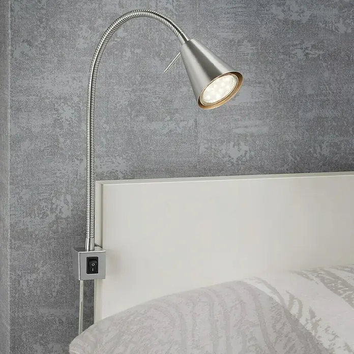 Briloner LED-Wandstrahler Tuso - 4 W, L x B x H: 5,8 x 21,7 x 40,3 cm, Warmweiß - Nahaufnahme einer modernen, silberfarbenen LED-Bettlampe mit flexiblem Arm, montiert an einem weißen Kopfteil.