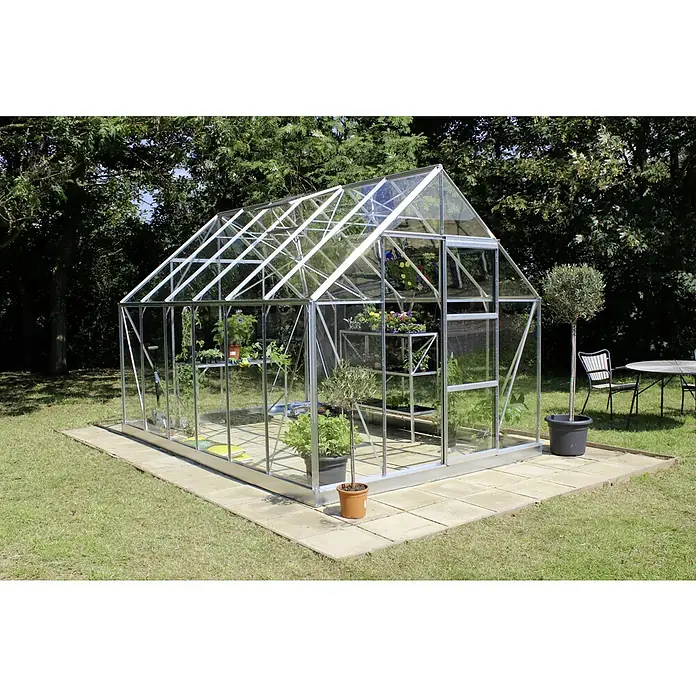 Halls Gewächshaus Universal 128 - Außenmaß inkl. Dachüberstand (B x T): 257 x 384 cm, Silber, Wandstärke: 3 mm - Geräumiges Gewächshaus auf einer gepflasterten Fläche mit Pflanzen darin und Pflanzen im Topf daneben.