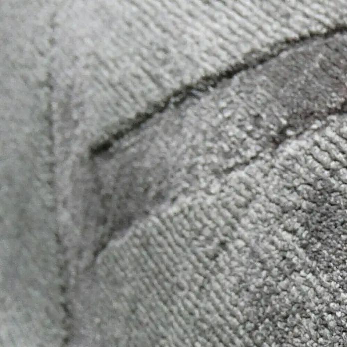 Kayoom Kurzflorteppich Luxury 310 - Grau, 150 x 80 cm, 100 % Viskose - Nahaufnahme eines grauen Sofas, das ein weiches und bequemes Aussehen mit seiner texturierten Oberfläche bietet.