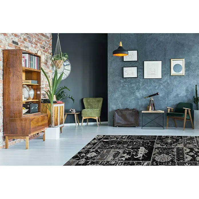 Kayoom Flachgewebeteppich River 150 - Schwarz/Grau, 150 x 80 cm, 70 % Baumwolle, 30 % Polyester - Ein Interieur mit einem dunklen Teppich mit orientalischen Motiven, einem Bücherregal und Sesseln in verschiedenen Grüntönen.
