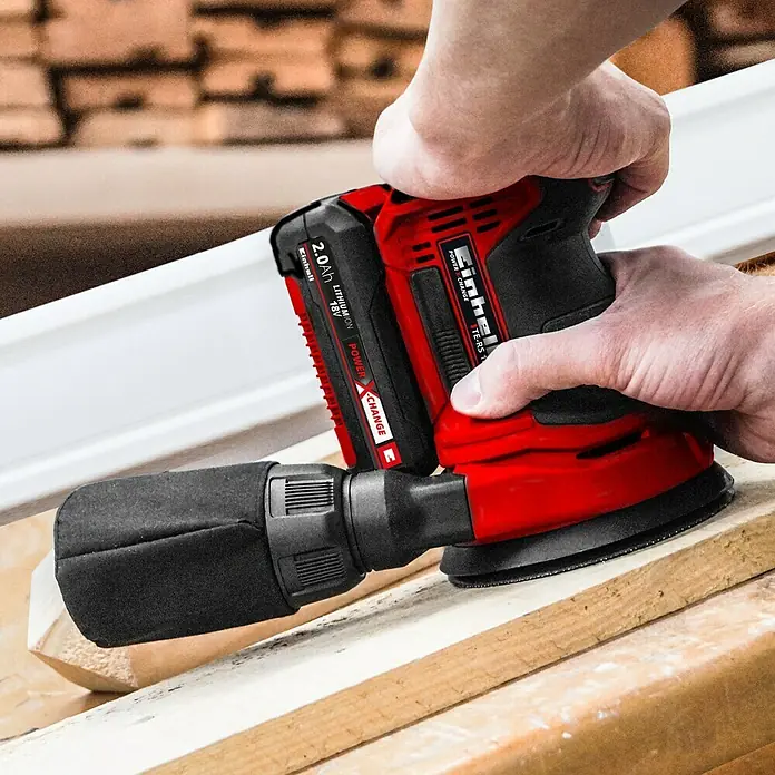 Einhell PXC 18V Lijadora excéntrica de batería TE-RS 18 Li-Solo -  - Primer plano de una lijadora rotoorbital inalámbrica Einhell TE-RS 18 Li roja y negra que se utiliza sobre un trozo de madera.