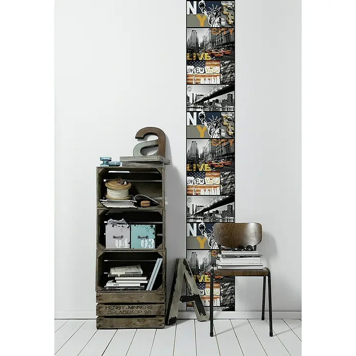 A.S. Création Designpanel pop.up - New York, Schwarz/Weiß/Bunt, 35 cm x 2,5 m - Wand mit New York-Motivtapete und Holzregal mit Deko-Objekten, dazu ein Stuhl mit Büchern gestapelt. Stilvolles Interieur für ein urbanes Ambiente.