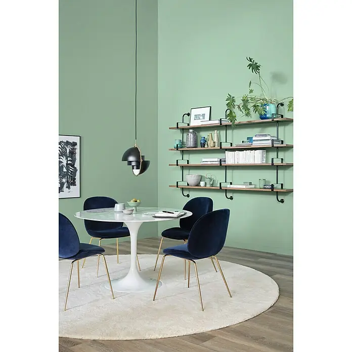 SCHÖNER WOHNEN-Farbe Wandfarbe Trendfarbe Limited Collection - Spa, Matt, 1 l, Konservierungsmittelfrei - Ein Esszimmer mit einem runden Tisch, blauen Samtstühlen und einer dekorativen Hängeleuchte unter Holzregalen an einer mintgrünen Wand.