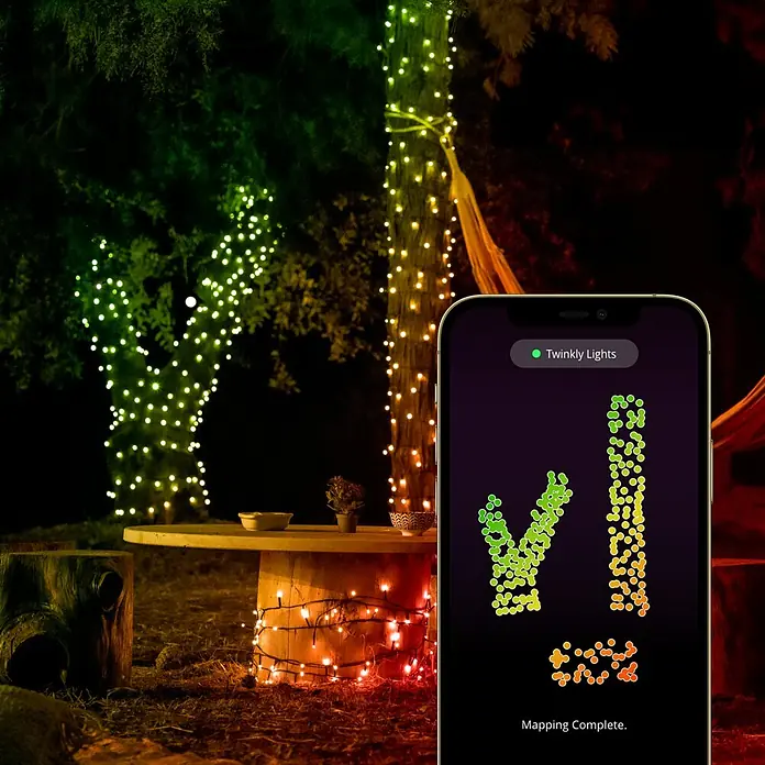 Twinkly Smart-LED-Lichterkette StringsAußen, 20 m, Lichtfarbe: RGBW, Anzahl Leuchtmittel: 250 Stk., Netzbetrieben - Blick auf die Twinkly Lichter, die einen Baum schmücken. Die Twinkly App mit der Lichtzuordnung wird auf einem Smartphone angezeigt.